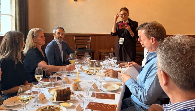 Dinner guests around a long table listening to a host speaking at a private event
